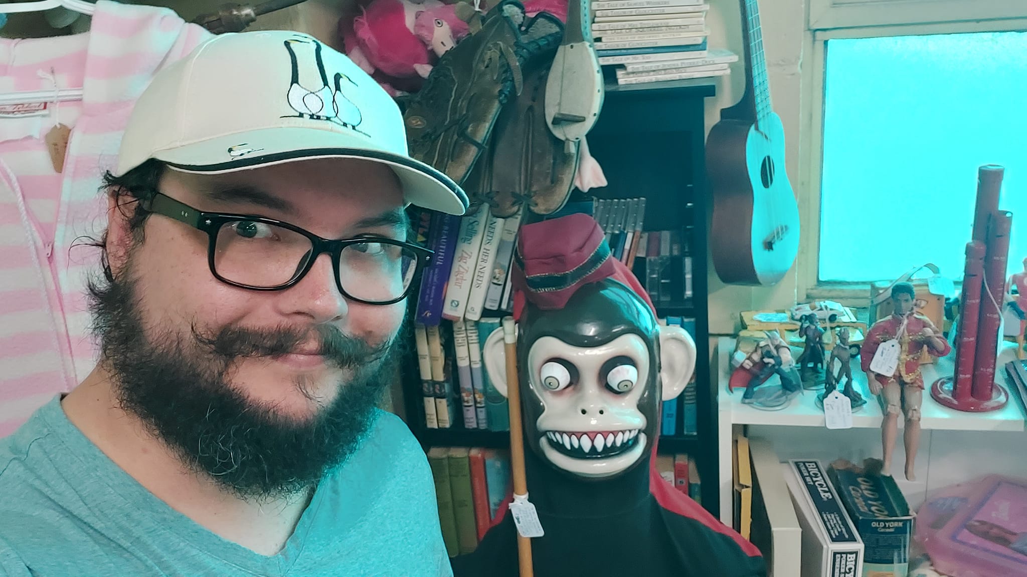 A man with short hair and bushy facial hair stands in an antique store, a sholder hight creepy monkey statue is centred in the frame